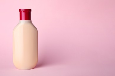 Photo of Bottle of shampoo on pale pink background, space for text