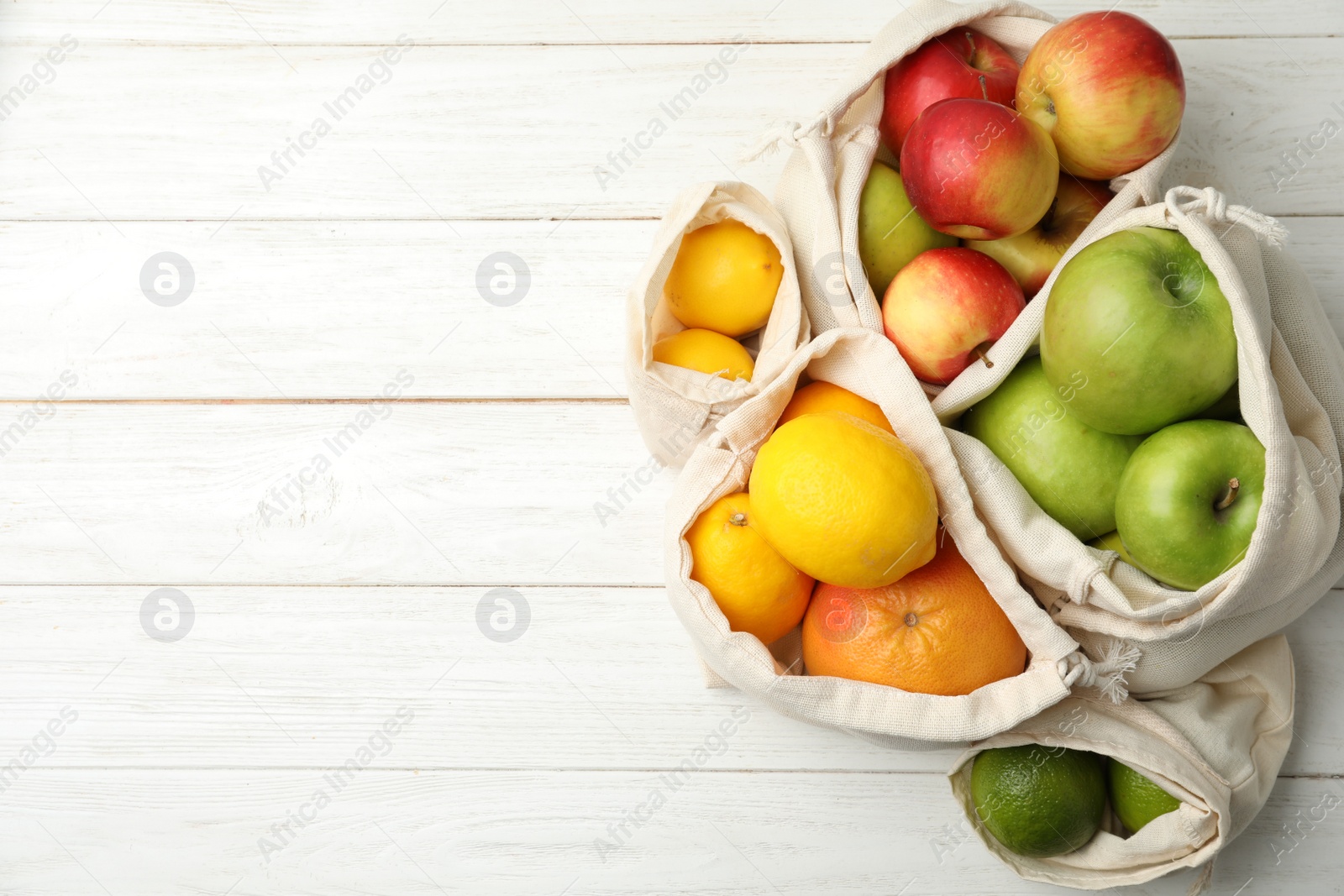Photo of Cotton eco bags with fruits on white wooden table, flat lay. Space for text