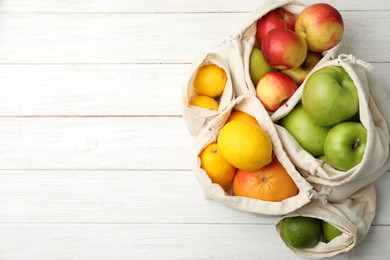 Cotton eco bags with fruits on white wooden table, flat lay. Space for text