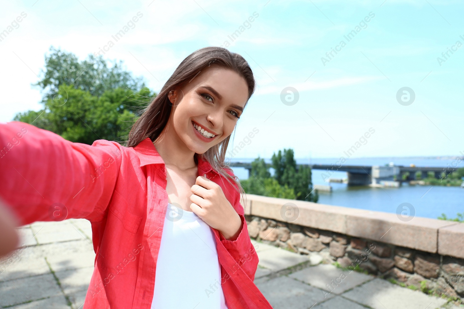 Photo of Happy young woman taking selfie on riverside. Space for text