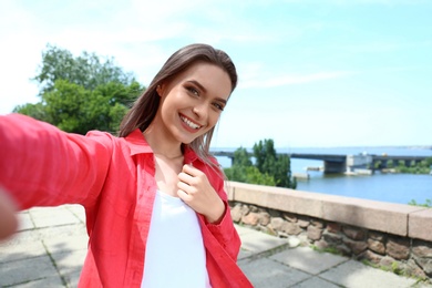 Photo of Happy young woman taking selfie on riverside. Space for text