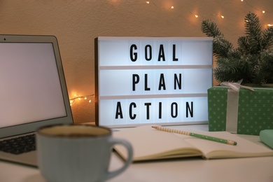 Photo of Light box with words Goal, Plan, Action near laptop and gift on table