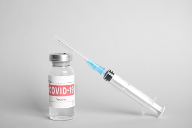 Vial with coronavirus vaccine and syringe on light background