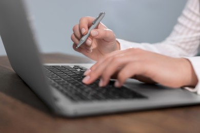 Photo of Woman with pen working on laptop at wooden table, closeup. Electronic document management