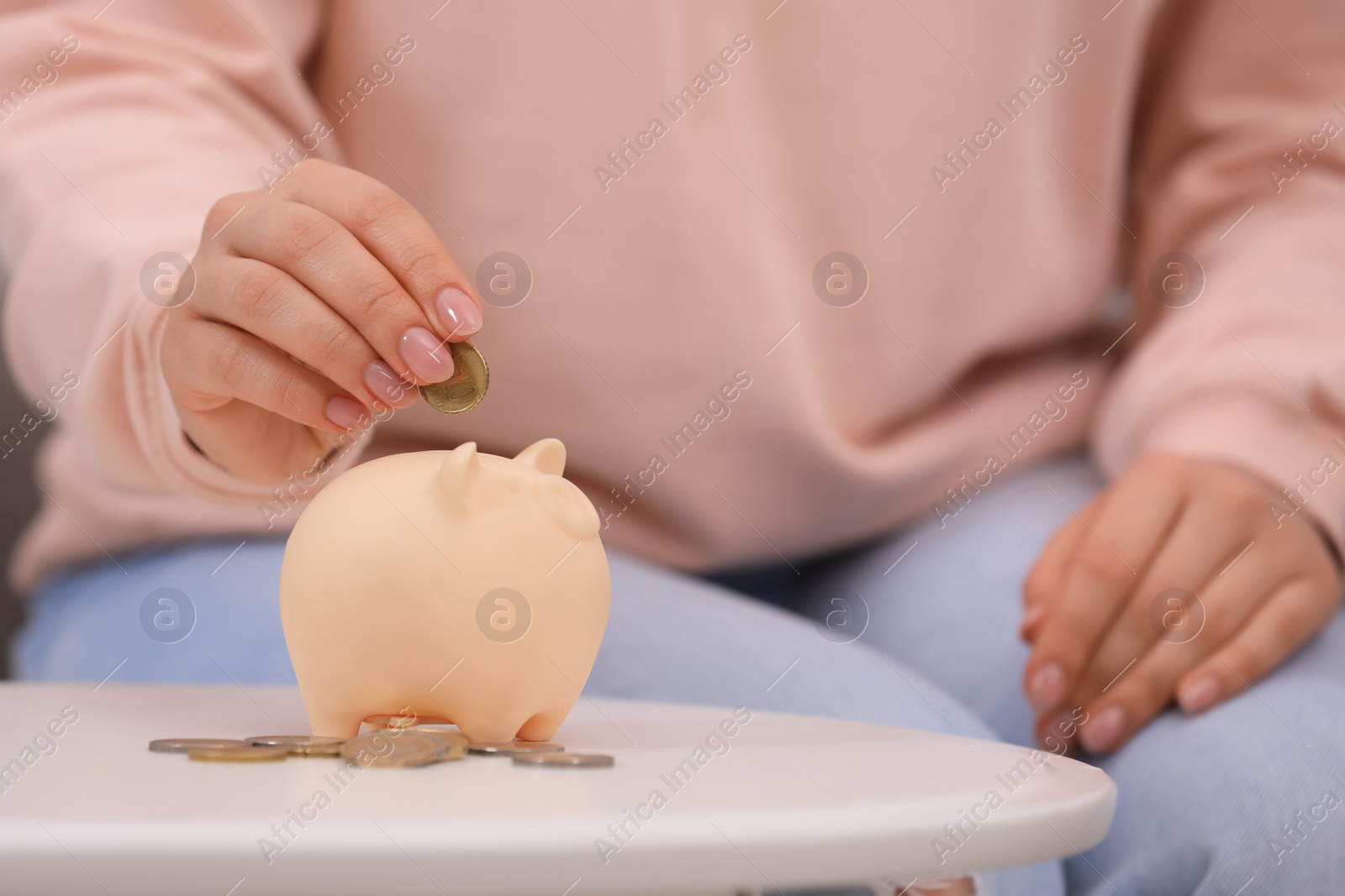 Photo of Young woman putting coin into piggy bank at table, closeup