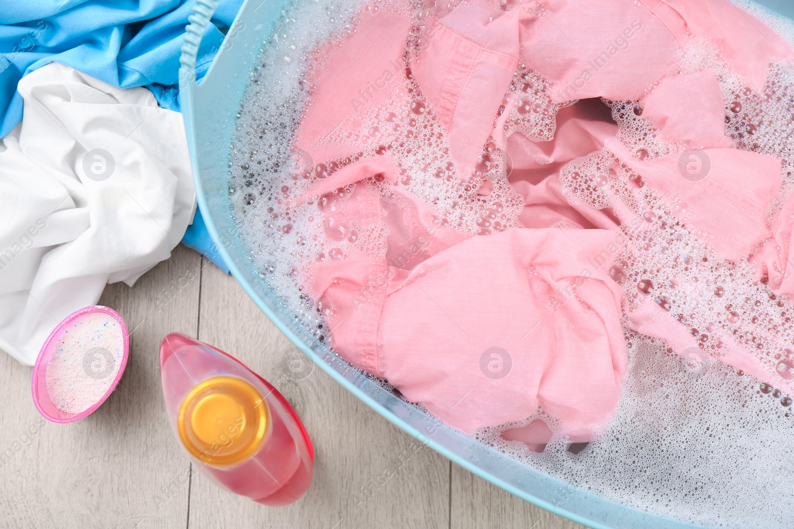 Photo of Basin with pink garment near bottle of detergent and powder on floor, flat lay. Hand washing laundry