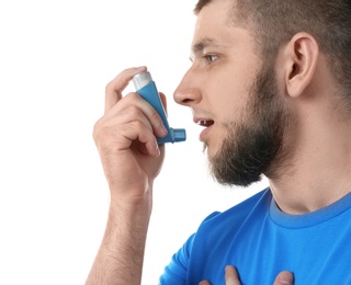 Young man using asthma inhaler on white background