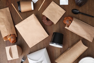 Flat lay composition with paper bags and different takeaway items on wooden background. Space for design