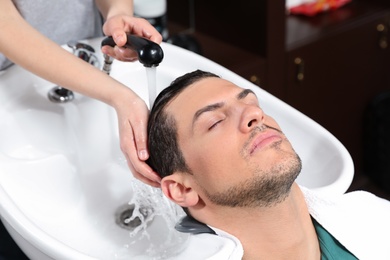 Photo of Stylist washing client's hair at sink in beauty salon