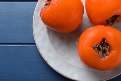 Photo of Delicious ripe persimmons on blue wooden table, top view. Space for text