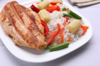 Grilled chicken breast and rice served with vegetables on white table, closeup