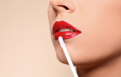 Photo of Beautiful woman applying red gloss on lips against color background, closeup. Space for text