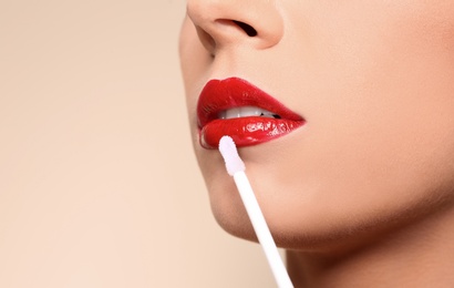 Beautiful woman applying red gloss on lips against color background, closeup. Space for text