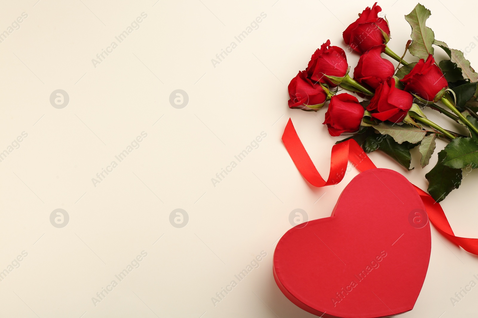 Photo of Beautiful red roses and heart shaped gift box on light background, flat lay with space for text. Valentine's Day celebration