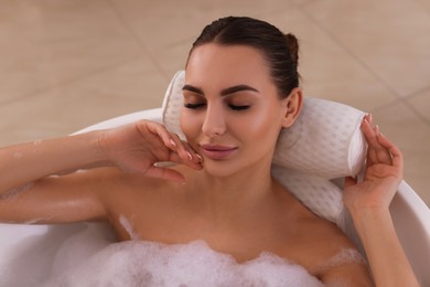 Photo of Young woman using pillow while enjoying bubble bath indoors