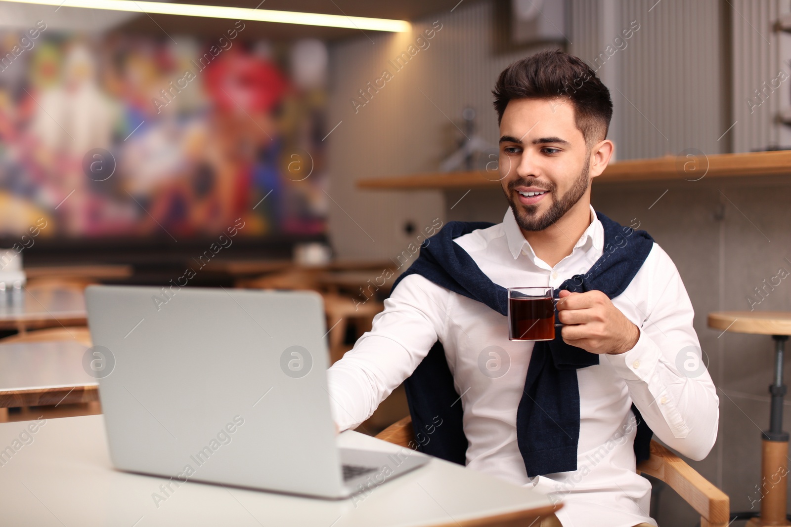 Photo of Young male business owner working with laptop in his cafe