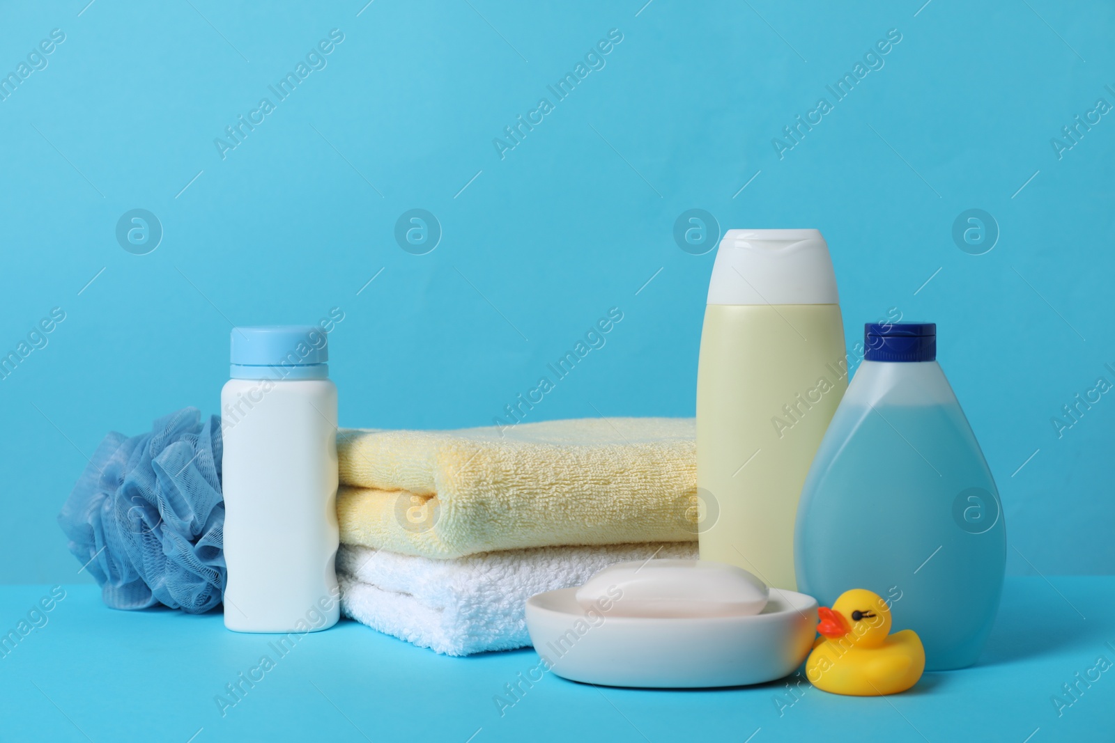 Photo of Baby cosmetic products, bath duck, sponge and towels on light blue background