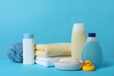 Photo of Baby cosmetic products, bath duck, sponge and towels on light blue background