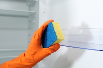 Photo of Worker in rubber gloves cleaning empty refrigerator, closeup