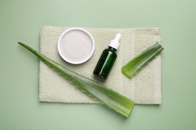 Cosmetic products, aloe leaves and towel on pale green background, top view