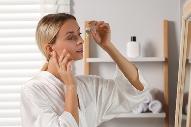 Photo of Beautiful woman applying cosmetic serum onto her face in bathroom