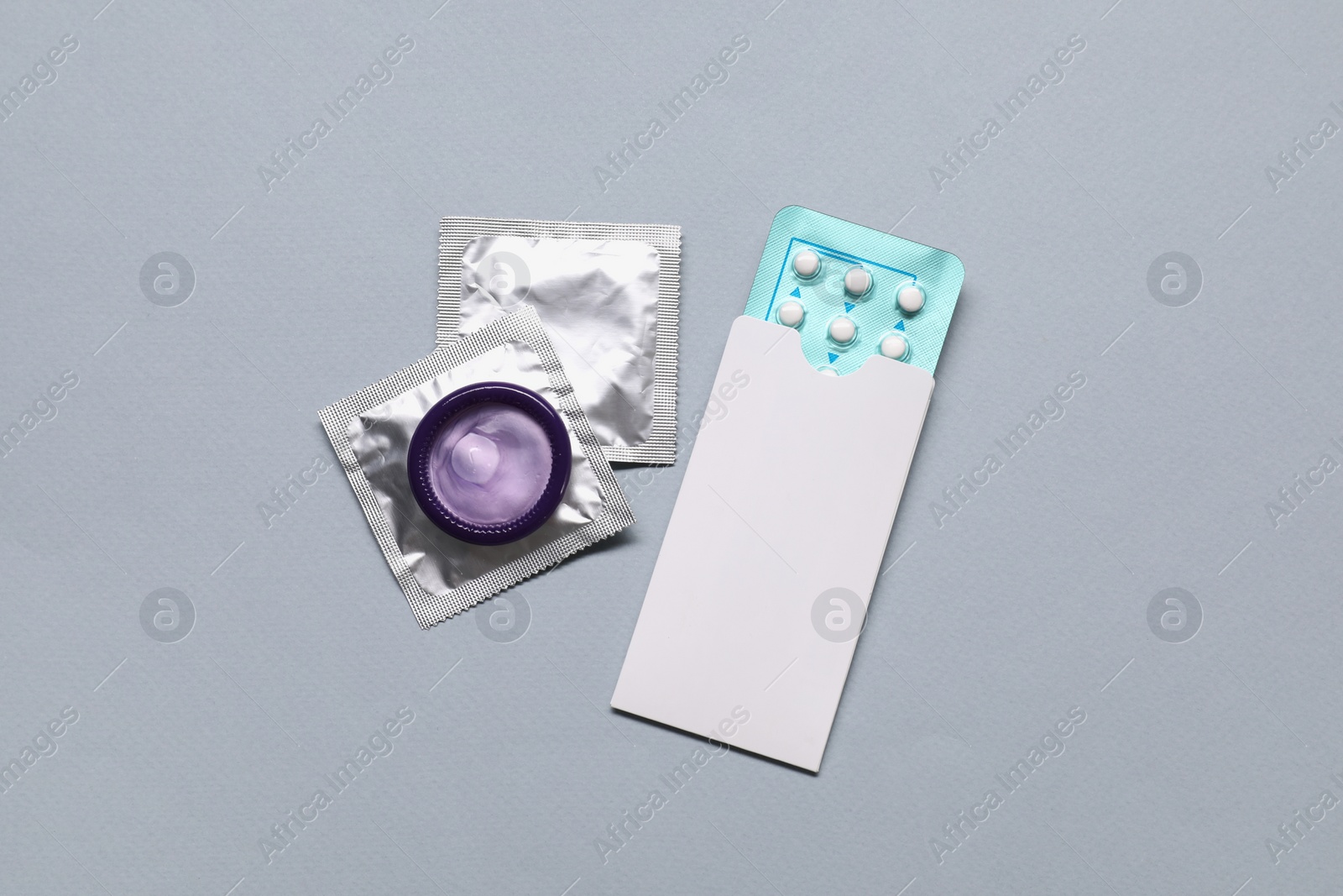 Photo of Contraception choice. Pills and condoms on grey background, flat lay