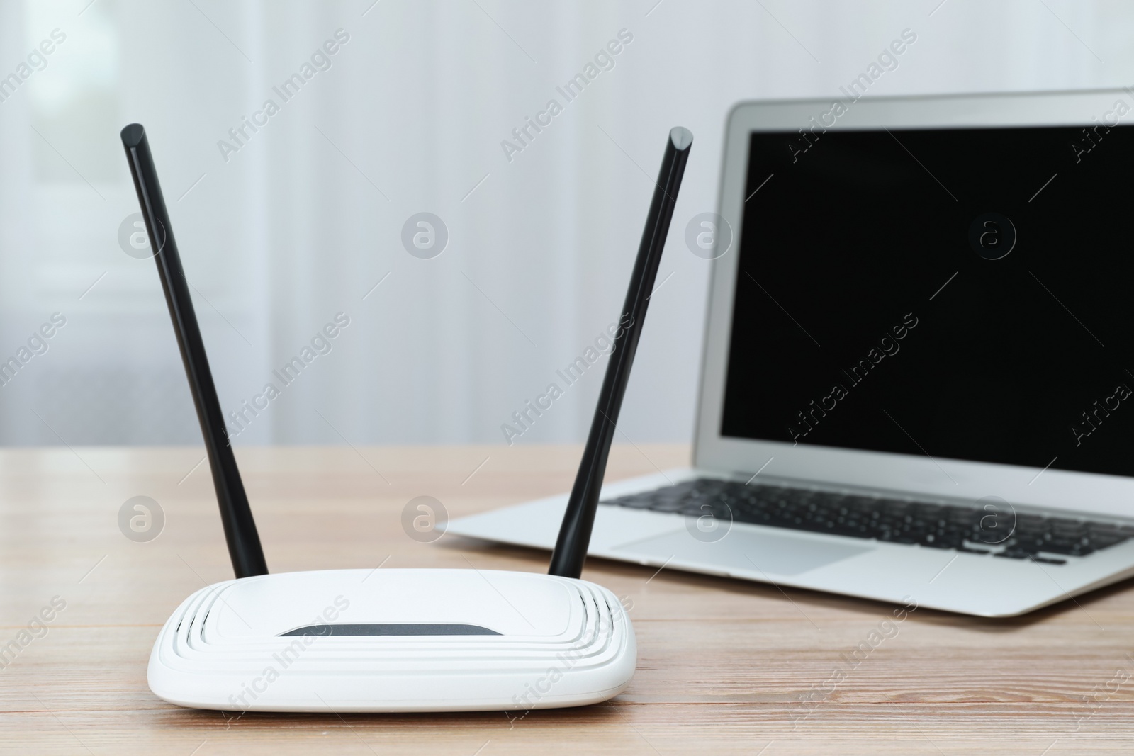 Photo of Modern Wi-Fi router and laptop on wooden table indoors