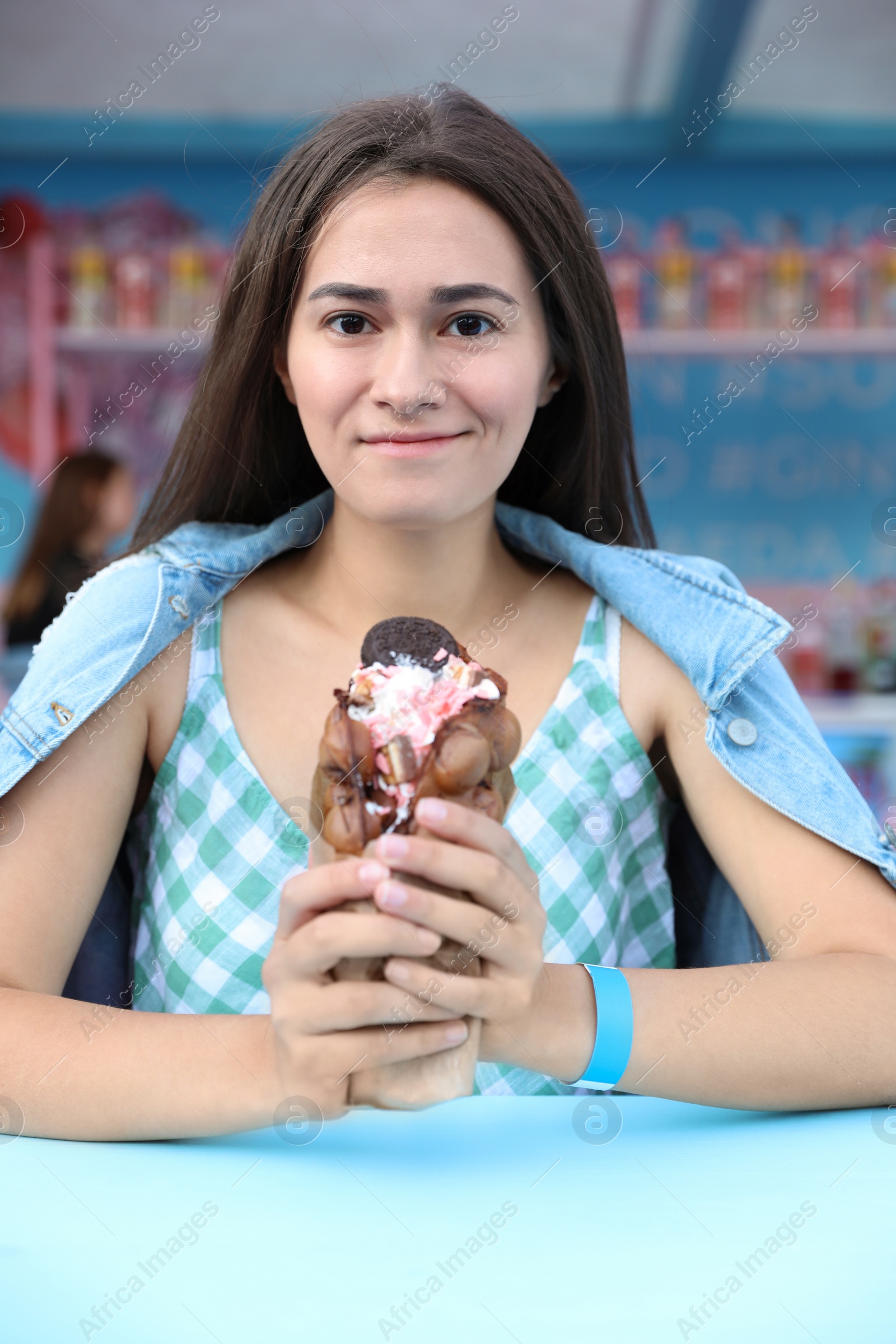 Photo of Pretty young woman holding delicious sweet bubble waffle with ice cream at table outdoors