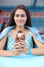 Photo of Pretty young woman holding delicious sweet bubble waffle with ice cream at table outdoors