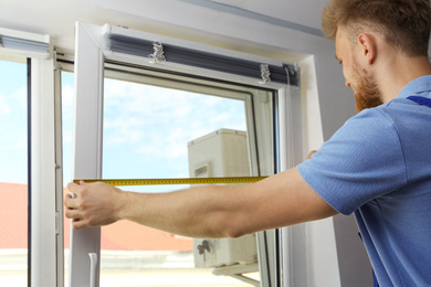 Image of Handyman with tape measure installing window blinds indoors