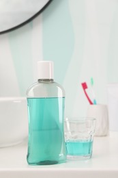 Photo of Bottle of mouthwash, toothbrushes and glass on white table in bathroom