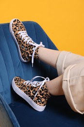 Photo of Woman posing in classic old school sneakers with leopard print and armchair on orange background, closeup