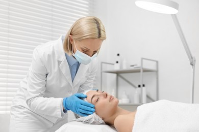 Dermatologist examining patient`s face under lamp in clinic