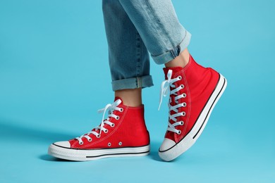 Woman in stylish gumshoes on light blue background, closeup