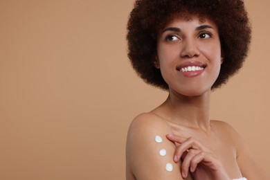 Photo of Beautiful young woman applying body cream onto arm on beige background, space for text