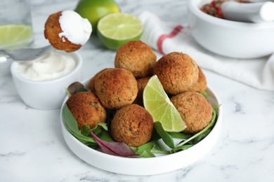 Photo of Delicious falafel balls with herbs and lime on white marble table