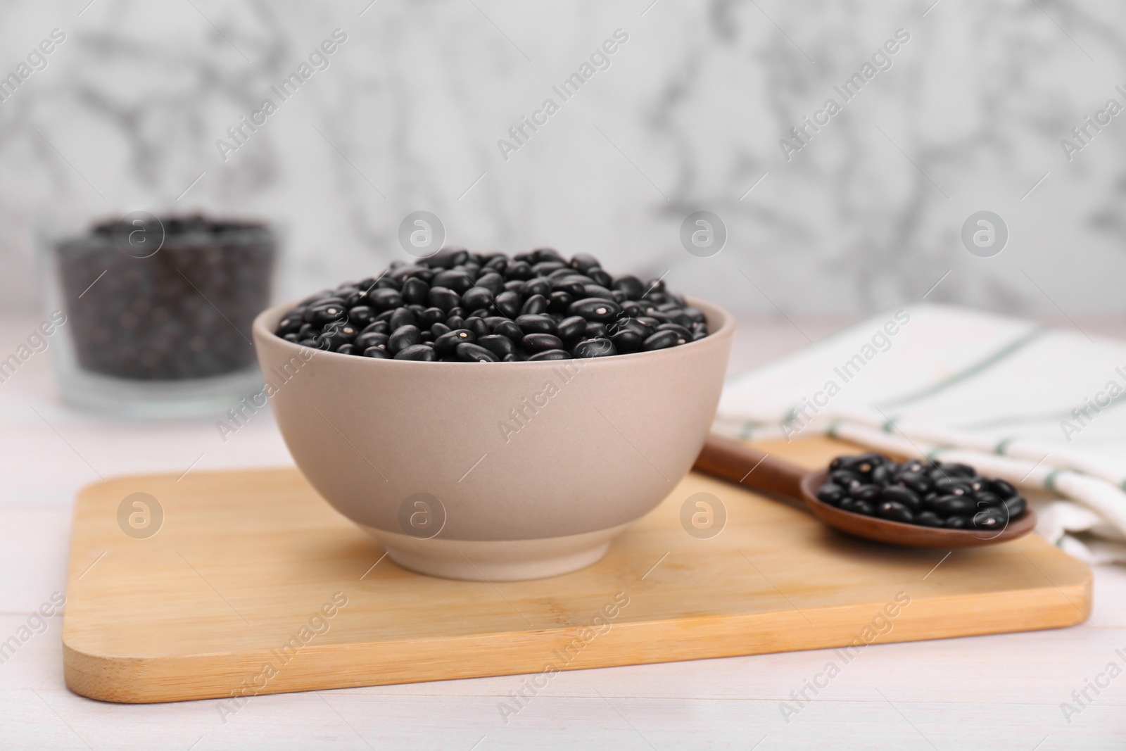 Photo of Bowl of raw black beans on white wooden table