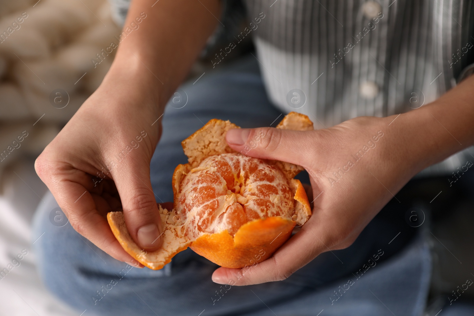 Photo of Woman peeling fresh tangerine on blurred background, closeup