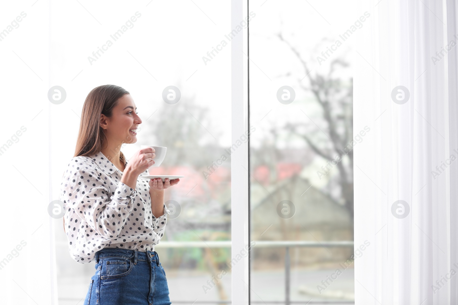 Photo of Young woman with cup near window indoors