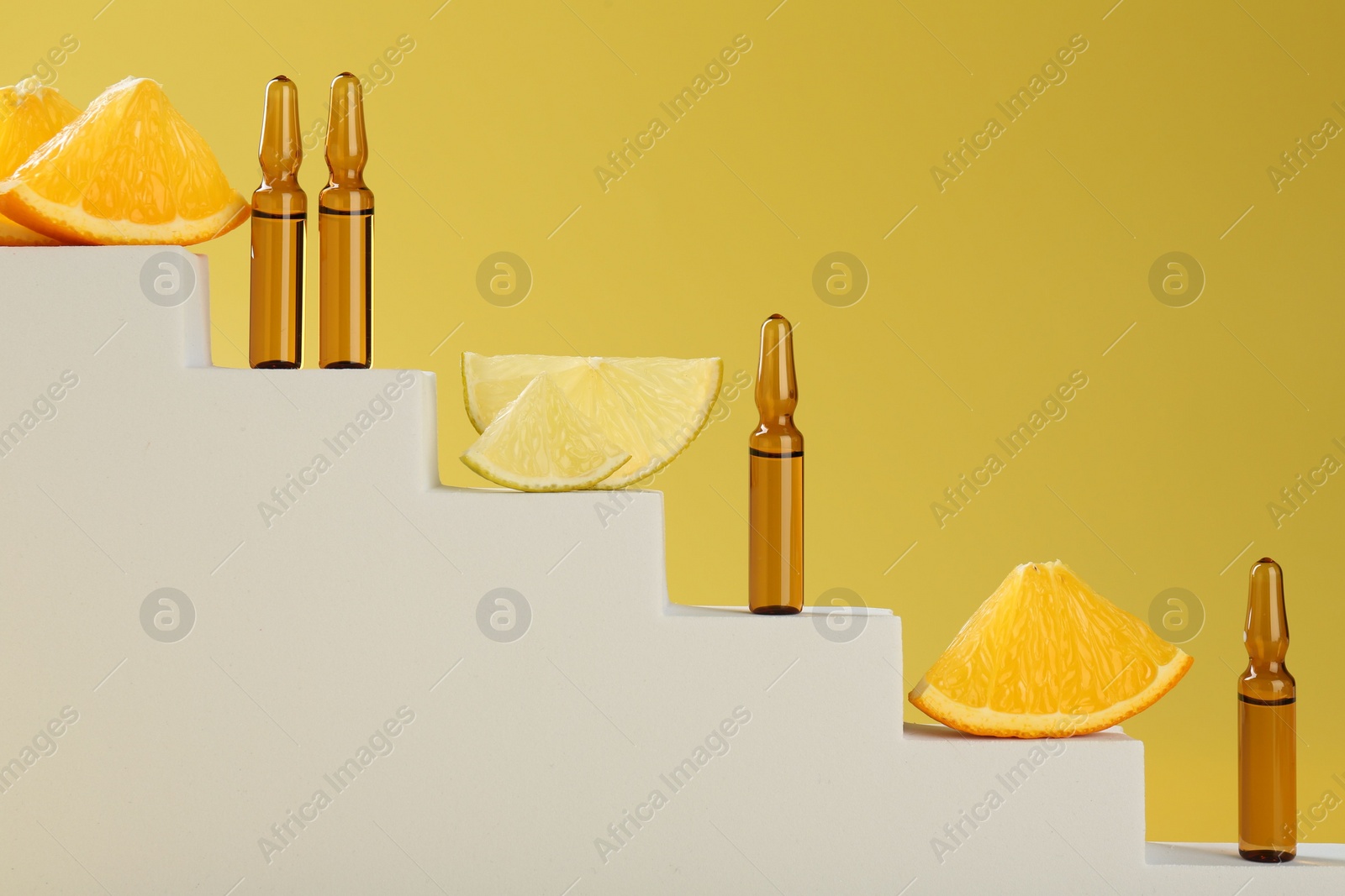 Photo of Stylish presentation of skincare ampoules with vitamin C and citrus slices on decorative stairs against yellow background, closeup