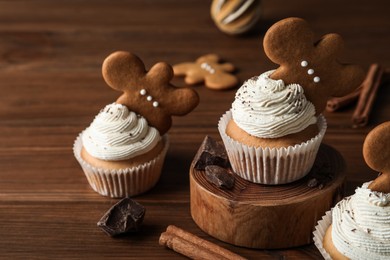 Photo of Tasty Christmas cupcakes with gingerbread man cookies on wooden table