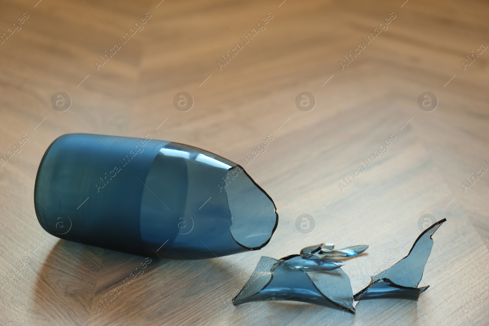 Photo of Broken blue glass vase on wooden floor, closeup