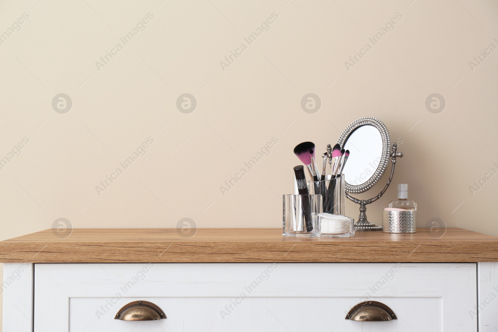 Photo of Organizer with makeup cosmetic products and mirror on table against light wall. Space for text