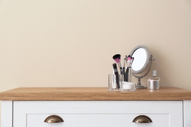 Photo of Organizer with makeup cosmetic products and mirror on table against light wall. Space for text