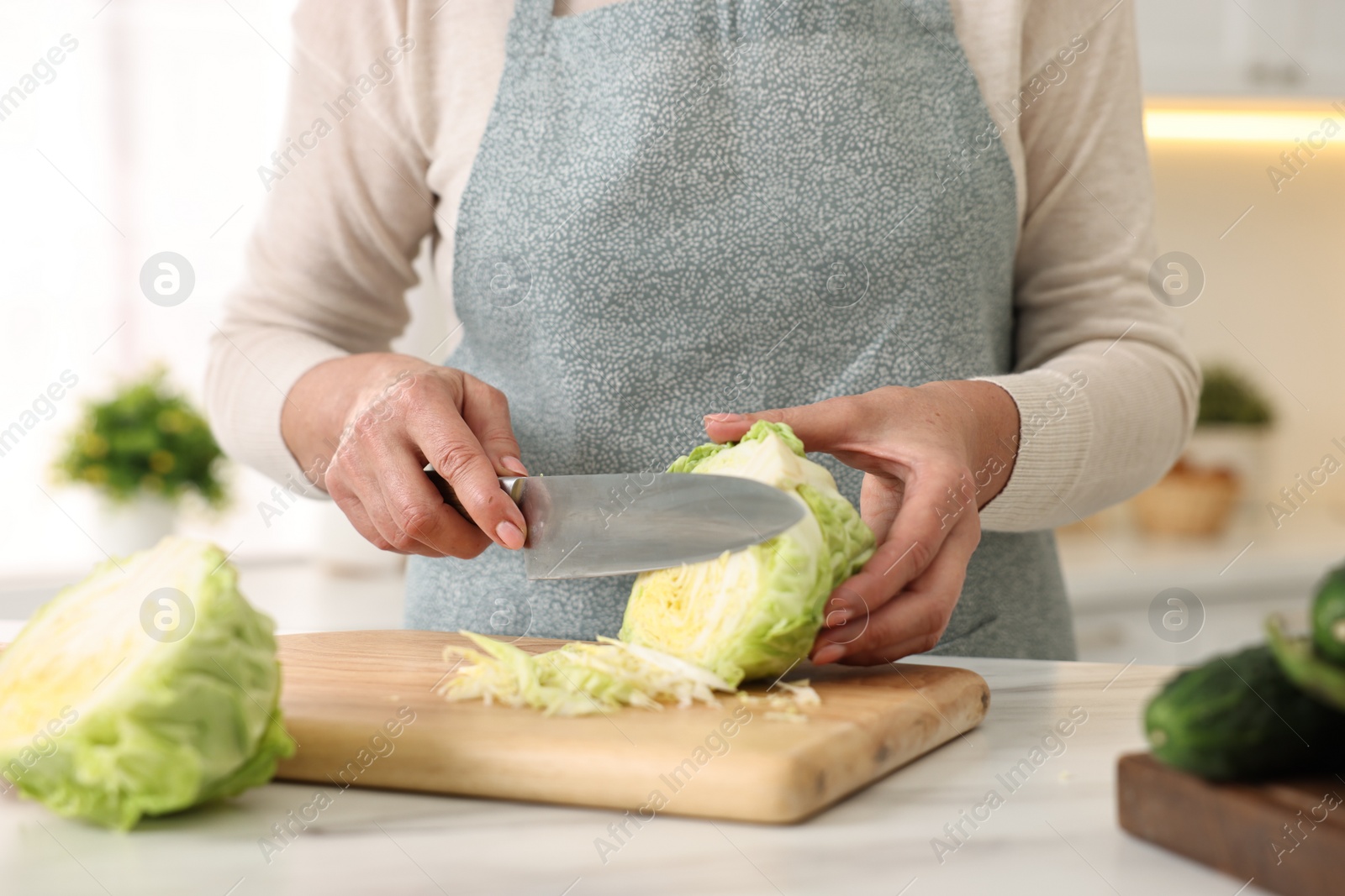 Photo of Housewife cutting cabbage at white marble table in kitchen, closeup