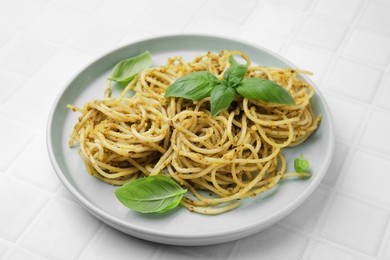 Photo of Delicious pasta with pesto sauce and basil on white tiled table, closeup
