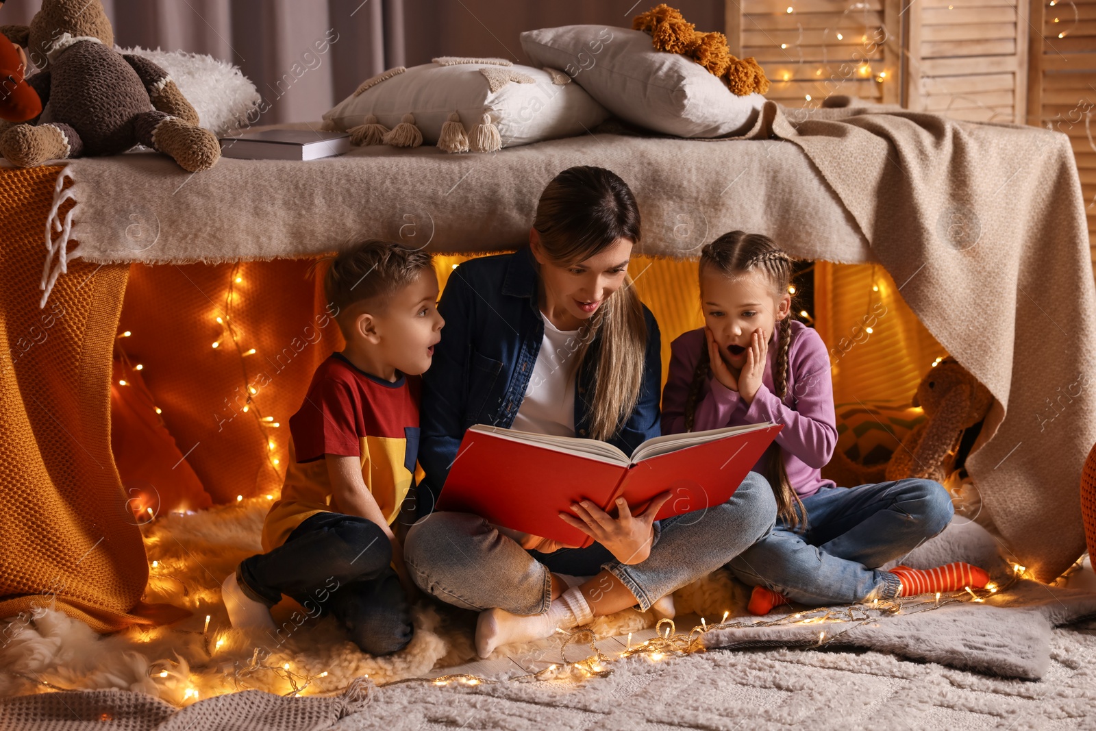 Photo of Mother and her children reading book in play tent at home