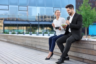 Photo of Smiling business people eating from lunch boxes outdoors. Space for text