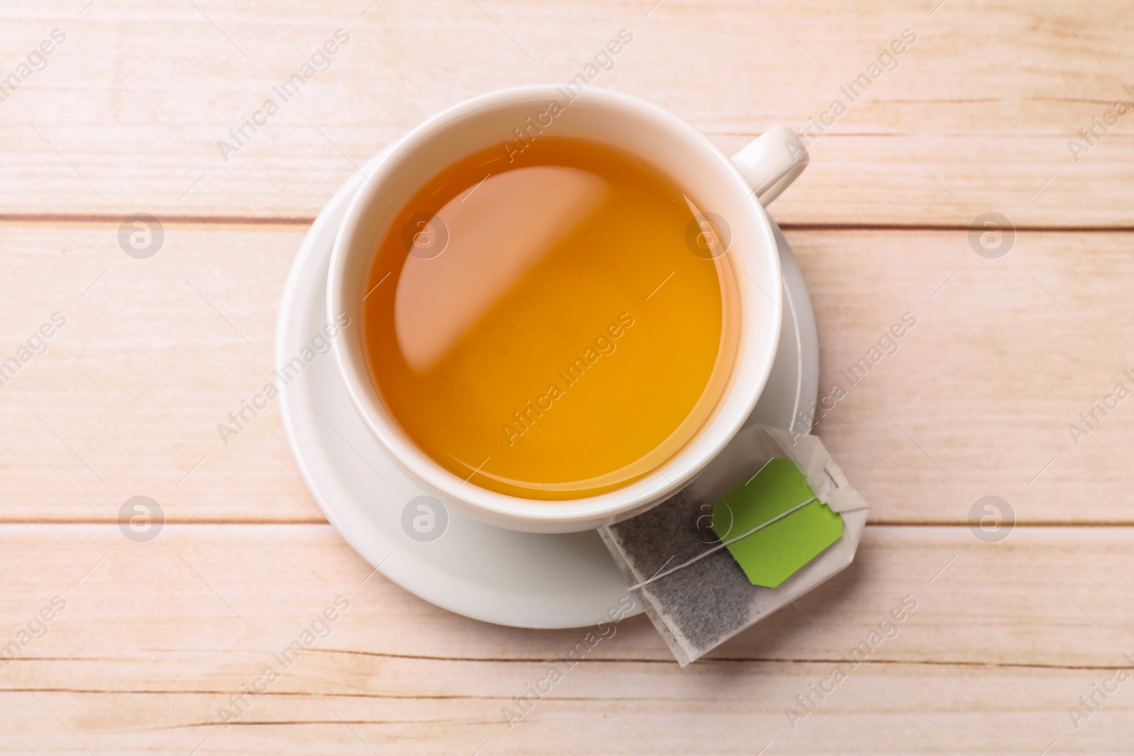 Photo of Tea bag and cup of hot beverage on light wooden table, top view