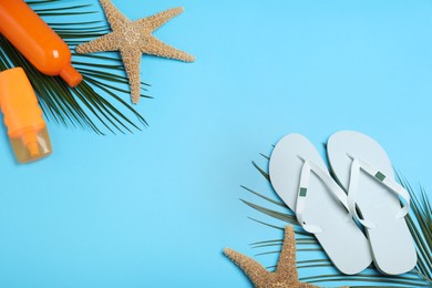 Stylish flip flops, sun protection products and starfish on light blue background, flat lay. Space for text